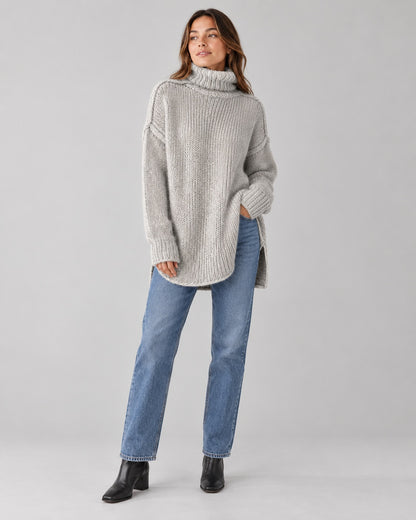 Woman wearing an oversized grey chunky knit turtleneck with straight-leg jeans and ankle boots