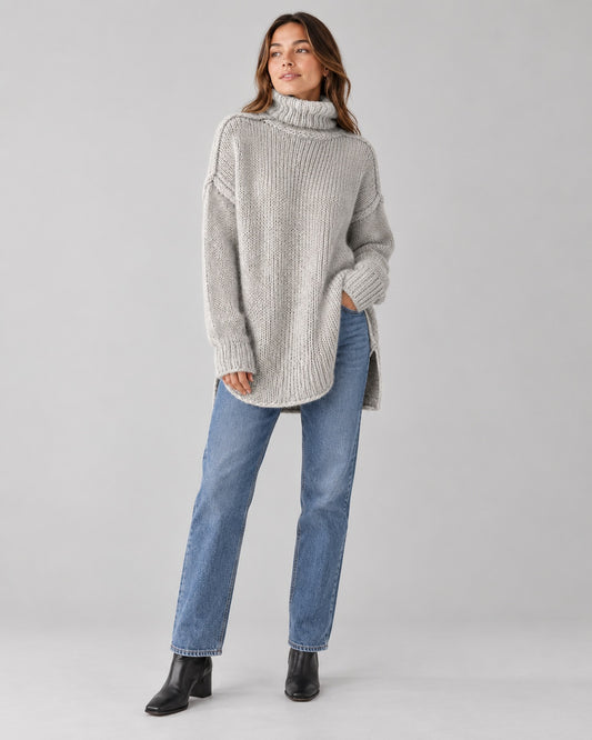 Woman wearing an oversized grey chunky knit turtleneck with straight-leg jeans and ankle boots