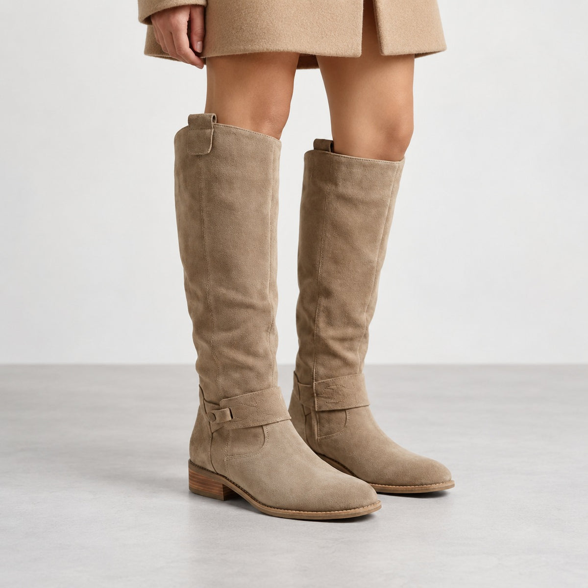 Beige suede-look knee-high slouch boots with low heel, worn with a camel coat